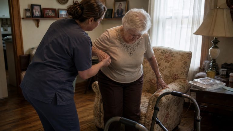 인디애나 가정에서 방문 요양사가 고령 여성의 보행을 돕는 모습 (Indiana home care aide assisting an elderly woman)
